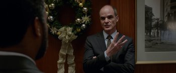 Movie still from “Secret in Their Eyes” (2015), directed by Billy Ray – A man in a business suit standing in front of a christmas wreath; Close Up shot, Over the shoulder angle