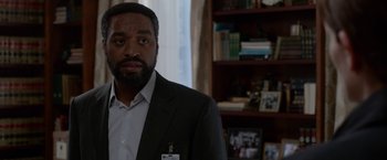 Movie still from “Secret in Their Eyes” (2015), directed by Billy Ray – A man wearing a suit and tie in a room; Close Up shot, Over the shoulder angle