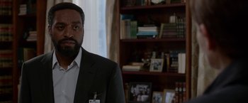 Movie still from “Secret in Their Eyes” (2015), directed by Billy Ray – A man wearing a suit and tie in a room; Close Up shot, Over the shoulder angle