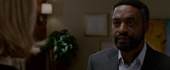 Movie still from “Secret in Their Eyes” (2015), directed by Billy Ray – A man wearing a suit and tie in a room; Close Up shot, Over the shoulder angle