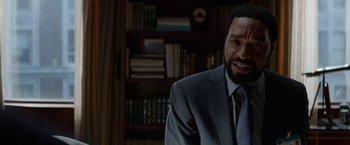 Movie still from “Secret in Their Eyes” (2015), directed by Billy Ray – A man wearing a suit and tie in a room with a bookshelf; Close Up shot, Over the shoulder angle