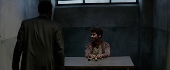 Movie still from “Secret in Their Eyes” (2015), directed by Billy Ray – A man sitting at a wooden table in front of another man; Medium shot, Over the shoulder angle