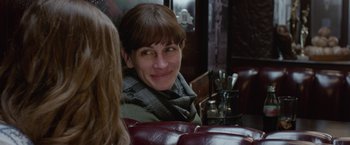 Movie still from “Secret in Their Eyes” (2015), directed by Billy Ray – A woman sitting at a table with a smile on her face; Close Up shot, Over the shoulder angle