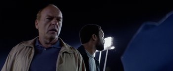 Movie still from “Secret in Their Eyes” (2015), directed by Billy Ray – Two men standing next to each other in front of a stadium; Close Up shot, Low angle
