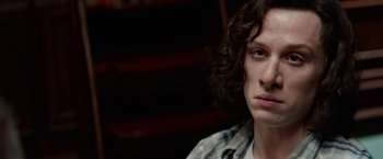 Movie still from “Secret in Their Eyes” (2015), directed by Billy Ray – A man with curly hair sitting in front of a bookshelf; Close Up shot, Low angle