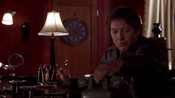 Movie still from “Secretary” (2002), directed by Steven Shainberg – A man sitting at a table in front of a lamp; Medium shot, Low angle