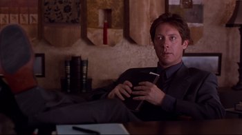 Movie still from “Secretary” (2002), directed by Steven Shainberg – A man in a suit and tie holding a cigarette; Medium shot, Over the shoulder angle