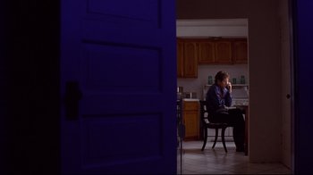 Movie still from “Secretary” (2002), directed by Steven Shainberg – A man sitting at a table in a kitchen; Wide shot, Low angle