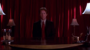 Movie still from “Secretary” (2002), directed by Steven Shainberg – A man wearing a suit and tie sitting at a table; Medium shot, Low angle