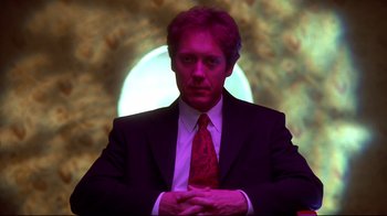 Movie still from “Secretary” (2002), directed by Steven Shainberg – A man wearing a suit and tie in front of a projection screen; Medium shot, Low angle