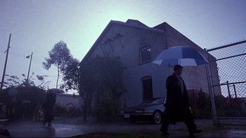 Movie still from “Secretary” (2002), directed by Steven Shainberg – A man walking down the street holding an umbrella; Extreme Wide shot, Low angle