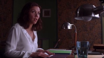 Movie still from “Secretary” (2002), directed by Steven Shainberg – A woman sitting at a table with papers in front of a lamp; Medium shot, Over the shoulder angle