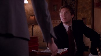 Movie still from “Secretary” (2002), directed by Steven Shainberg – A man wearing a suit and tie sitting at a table; Medium shot, Over the shoulder angle