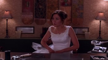 Movie still from “Secretary” (2002), directed by Steven Shainberg – A woman sitting at a table in a white dress; Medium shot, Over the shoulder angle