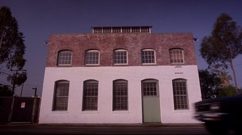 Movie still from “Secretary” (2002), directed by Steven Shainberg – A white building with a green door on the side of the building; Extreme Wide shot, Low angle
