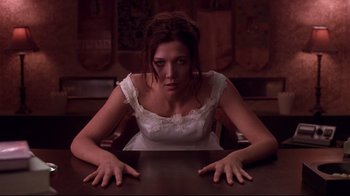 Movie still from “Secretary” (2002), directed by Steven Shainberg – A woman sitting at a table with her hands over her face; Medium shot, Low angle