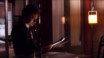 Movie still from “Secretary” (2002), directed by Steven Shainberg – A man sitting at a table reading a newspaper; Medium shot, Low angle