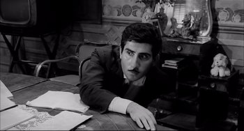 Movie still from “Seduced and Abandoned” (1964), directed by Pietro Germi – A black and white photo of a man sitting at a table; Medium shot, High angle