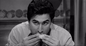 Movie still from “Seduced and Abandoned” (1964), directed by Pietro Germi – A black - and - white photo of a man taking a bite out of a donut; Close Up shot, Overhead angle