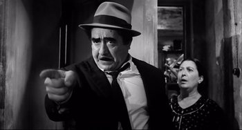 Movie still from “Seduced and Abandoned” (1964), directed by Pietro Germi – An older man wearing a hat and a suit points at a woman; Medium shot, Low angle