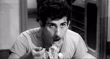 Movie still from “Seduced and Abandoned” (1964), directed by Pietro Germi – A black - and - white photo of a man eating food; Close Up shot, High angle