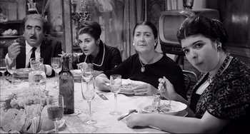 Movie still from “Seduced and Abandoned” (1964), directed by Pietro Germi – A group of people sitting at a dinner table; Medium shot, High angle