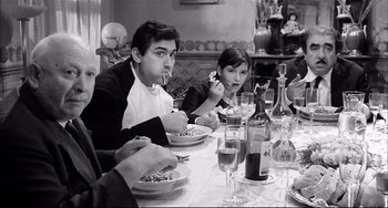 Movie still from “Seduced and Abandoned” (1964), directed by Pietro Germi – A group of people sitting at a dinner table; Medium shot, High angle