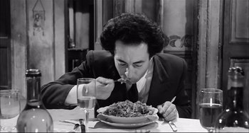 Movie still from “Seduced and Abandoned” (1964), directed by Pietro Germi – A man sitting at a table eating a plate of food; Medium shot, High angle