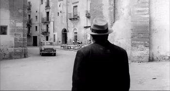 Movie still from “Seduced and Abandoned” (1964), directed by Pietro Germi – A man wearing a hat is walking down the street; Wide shot, Low angle