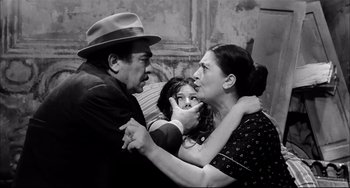 Movie still from “Seduced and Abandoned” (1964), directed by Pietro Germi – An old photo of a man and a woman and a little girl; Medium shot, High angle