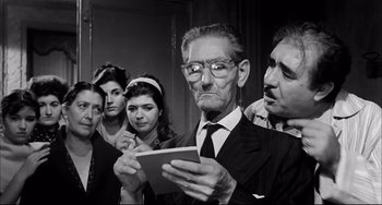 Movie still from “Seduced and Abandoned” (1964), directed by Pietro Germi – An old man in a suit and tie looking at a piece of paper; Medium shot, Low angle