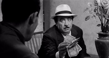 Movie still from “Seduced and Abandoned” (1964), directed by Pietro Germi – A man in a suit and a white hat is holding money; Close Up shot, Over the shoulder angle