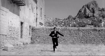 Movie still from “Seduced and Abandoned” (1964), directed by Pietro Germi – A man running through a field in front of a stone wall; Wide shot, Low angle