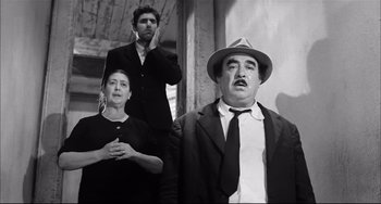 Movie still from “Seduced and Abandoned” (1964), directed by Pietro Germi – A man and a woman standing next to a man in a hat; Medium shot, Low angle