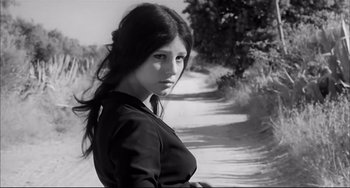 Movie still from “Seduced and Abandoned” (1964), directed by Pietro Germi – A woman standing on the side of a dirt road; Close Up shot, Low angle