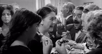 Movie still from “Seduced and Abandoned” (1964), directed by Pietro Germi – A group of people sitting around a table eating food; Medium shot, Over the shoulder angle