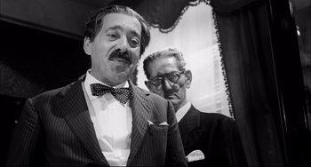 Movie still from “Seduced and Abandoned” (1964), directed by Pietro Germi – A man in a suit and tie next to another man in a suit and tie; Medium shot, Low angle
