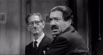 Movie still from “Seduced and Abandoned” (1964), directed by Pietro Germi – A black - and - white photo of two men in suits; Close Up shot, Low angle