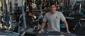 Movie still from “Seeking a Friend for the End of the World” (2012), directed by Lorene Scafaria – A man standing in front of a weight machine; Medium shot, Over the shoulder angle