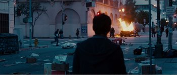 Movie still from “Seeking a Friend for the End of the World” (2012), directed by Lorene Scafaria – A man standing on the side of a road near a fire; Extreme Wide shot, Over the shoulder angle