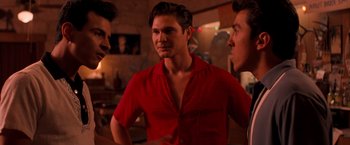Movie still from “Selena” (1997), directed by Gregory Nava – A man in a red shirt is standing next to two other men; Medium shot, Over the shoulder angle