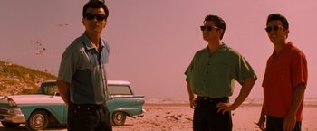 Movie still from “Selena” (1997), directed by Gregory Nava – Two men standing on the beach with a car in the background; Medium shot, Low angle