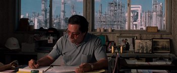 Movie still from “Selena” (1997), directed by Gregory Nava – A man sitting at a table in front of an oil refinery; Medium shot, Low angle