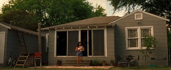 Movie still from “Selena” (1997), directed by Gregory Nava – A woman standing in front of a house; Wide shot, Low angle