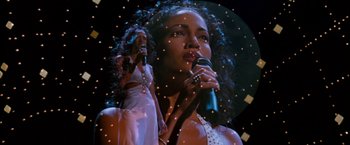 Movie still from “Selena” (1997), directed by Gregory Nava – A woman holding a microphone in front of a picture of herself; Medium shot, Low angle