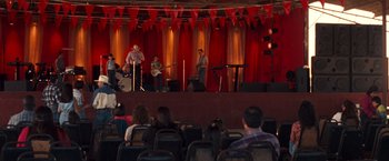 Movie still from “Selena” (1997), directed by Gregory Nava – A group of people sitting on a stage with musical instruments; Wide shot, Over the shoulder angle