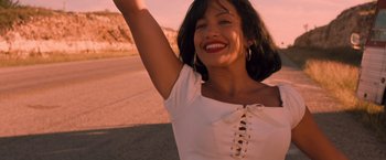 Movie still from “Selena” (1997), directed by Gregory Nava – A beautiful young lady smiling while standing next to a road; Close Up shot, Low angle