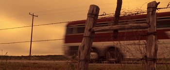 Movie still from “Selena” (1997), directed by Gregory Nava – A red bus driving down a road next to barbed wire fence; Wide shot, Low angle