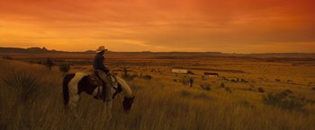 Movie still from “Selena” (1997), directed by Gregory Nava – A man riding a horse in a field at sunset; Extreme Wide shot, Low angle