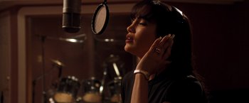 Movie still from “Selena” (1997), directed by Gregory Nava – A woman with her hand to her ear in front of a microphone in a recording studio; Close Up shot, Low angle